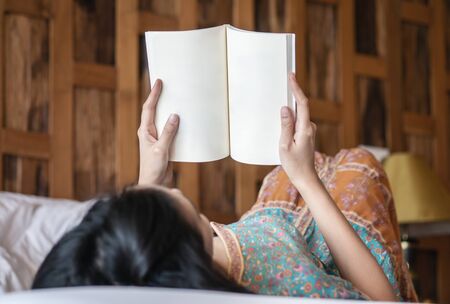 Closeup woman reading a book on bed in her bedroom in the morningの写真素材