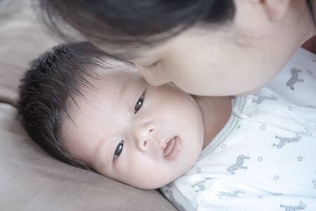 Closeup a baby on bed with her mother give a kissの写真素材