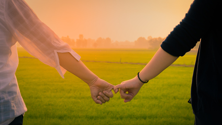 Close up Two Asian women wearing white and black shirts stand  
be hand in hand  and look at the green Field morning light.の写真素材