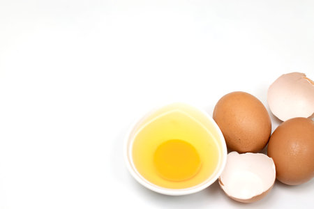 Egg yolk in a white bowl and eggshell and two eggs on a white background and copy space