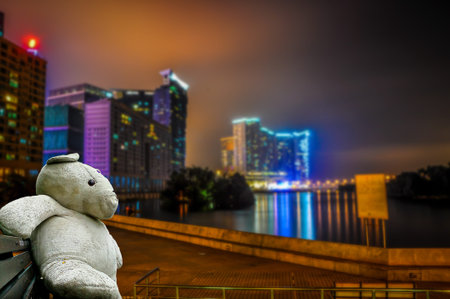 Big white teddy bears sitting on a wooden chair with  Colorful light from the light building in the capital. ASEAN Tourism.の写真素材