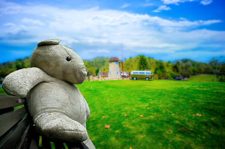 Big white teddy bears sitting on a wooden chair with  Lawn Farm in a van and a beautiful sky.の写真素材