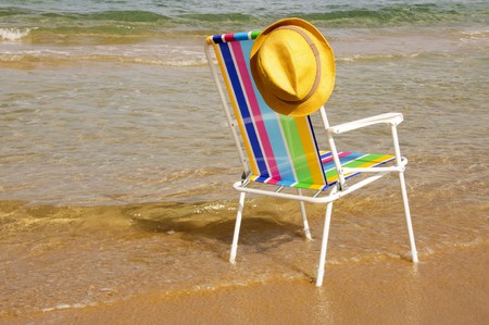 a colored deckchair and a straw hat on the beachの写真素材