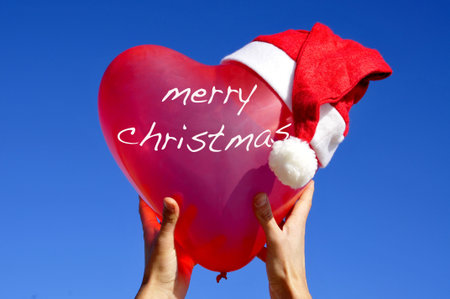 merry christmas written in a heart-shaped balloon with a santa hat