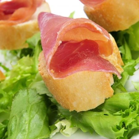 slices of bread with spanish serrano ham served as tapas over a pile of lettuce leavesの写真素材