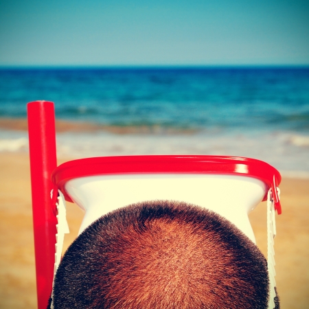 picture from the back of a man wearing a diving mask and a snorkel on the beach, with a retro effectの写真素材