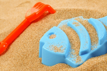 a blue fish-shaped mold and an orange toy shovel on the sandの写真素材