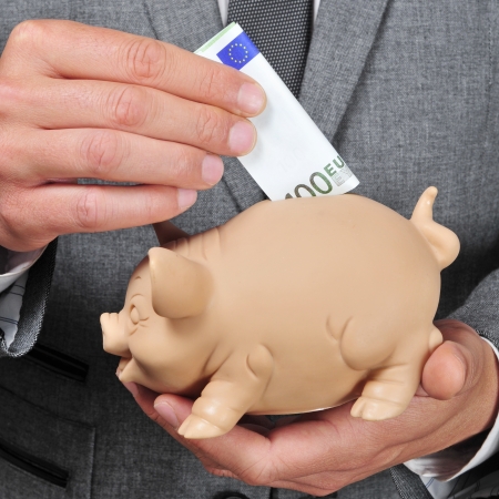 closeup of a man wearing a suit introducing a euro bill in a piggy bankの写真素材