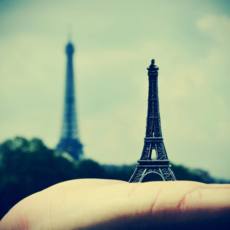 picture of someone holding a reproduction of the Eiffel Tower with the real Eiffel Tower in the background, in Paris, France, with a retro effectの写真素材