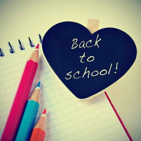 sentence back to school written in a heart-shaped blackboard and some pencil crayons of different colors on a notebook, with a retro effectの写真素材