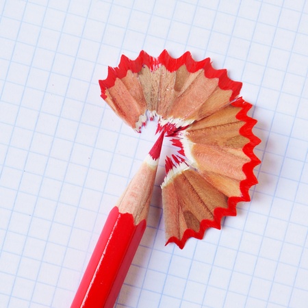 a sharpened red coloured pencil with its shavings on a checkered paper sheetの写真素材