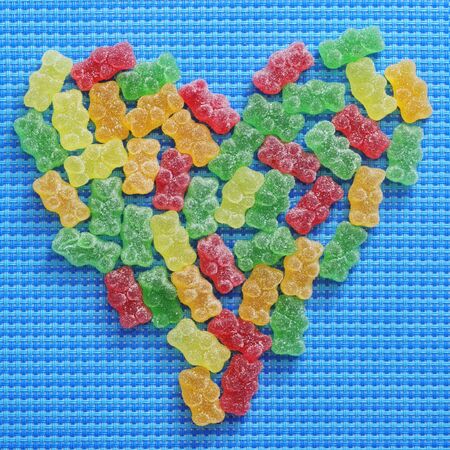 gummy bears of different colors forming a heart on a blue woven backgroundの写真素材