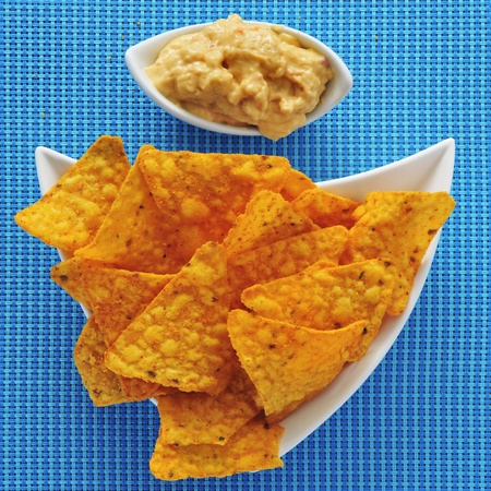 a plate with tortilla chips and a bowl with hummus, on a blue fabric backgroundの写真素材
