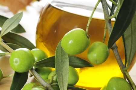 closeup of a branch of olive tree with olives and a bottle of olive oil in the backgroundの写真素材