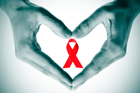 man hands forming a heart with his hands and a red ribbon for the fight against AIDS on a white...