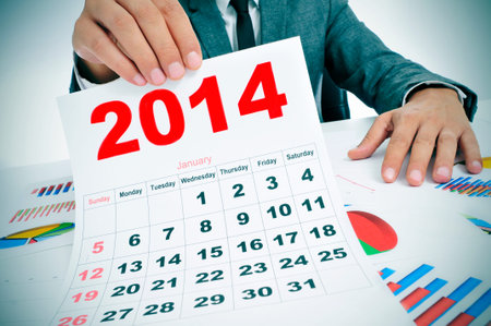 man wearing a suit sitting in a desk with a pile of charts and showing a 2014 calendarの写真素材