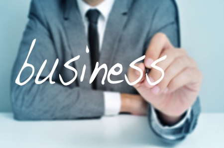 man wearing a suit sitting in a table writing the word business in the foregroundの写真素材