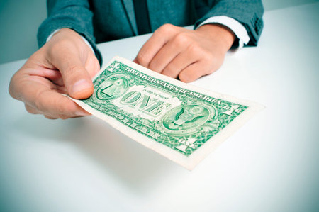 a man wearing a suit sitting in a desk offering a one US dollar billの写真素材