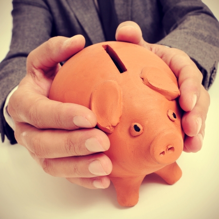 a man wearing a suit sitting in a desk with a piggy bank in his handsの写真素材