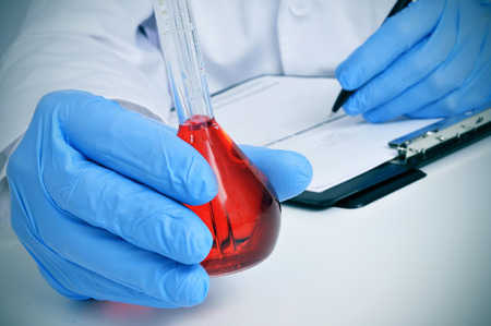 man in white coat with a volumetric flask with a red liquid in a laboratoryの写真素材