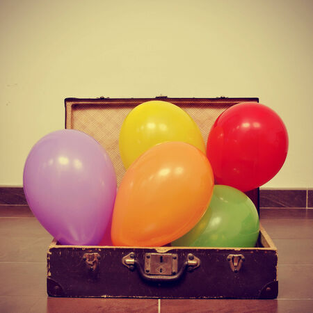 picture of a pile of balloons of different colors in an old suitcase, with a retro effectの写真素材