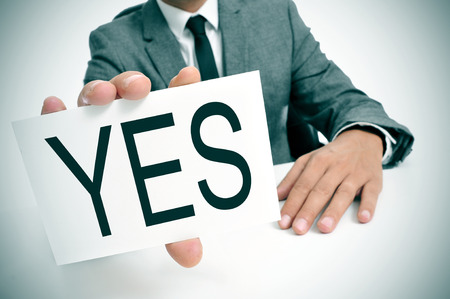 man wearing a suit sitting in a table showing a signboard with the word yes written in itの写真素材