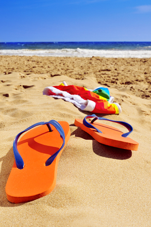 orange flip-flops and colorful swimsuit in the sand of a beachの写真素材