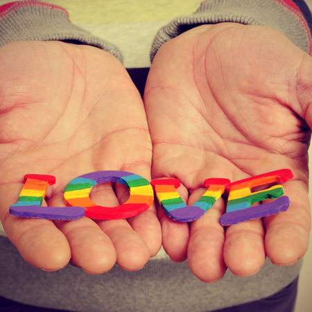 a young man holding in his hands letters painted as the gay pride flag forming the word love, with a retro effectの写真素材