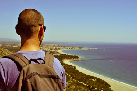 young man with a backpack looking at the seaの写真素材