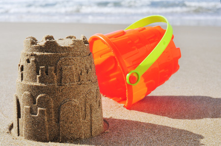 an orange toy bucket and a sandcastle on the sand of a beachの写真素材