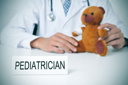 a doctor sitting in a desk with a injured teddy bear and a nameplate with the word pediatrician written in itの写真素材