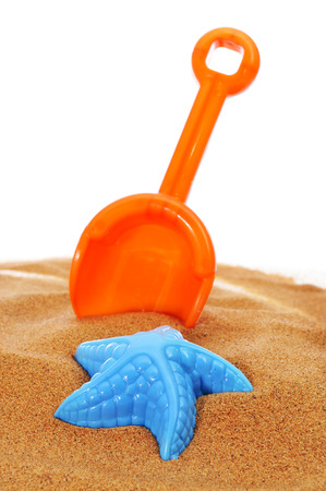 an orange toy shovel and a blue starfish-shaped mould on the sand, on a white backgroundの写真素材