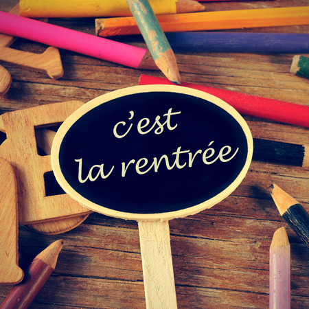 the sentence c'est la rentree, back to school written in french in a blackboard label, on a wooden table and colored pencils of different colorsの写真素材