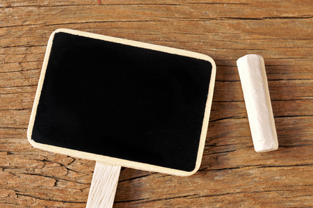 a blank chalkboard label and a piece chalk on a rustic wooden backgroundの写真素材