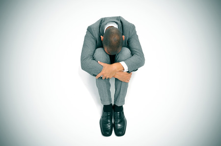 a businessman curled up in the floor with his head between his kneesの写真素材