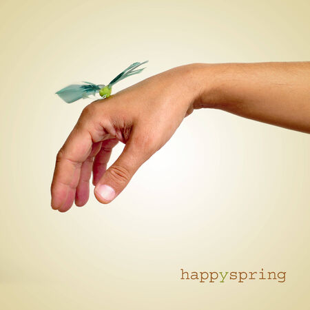 a fake butterfly landed in the hand of a young man and the sentence happy spring on a beige backgroundの写真素材