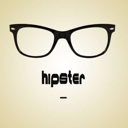 the word hipster and a black plastic rimmed eyeglasses on a beige background with a retro effectの写真素材