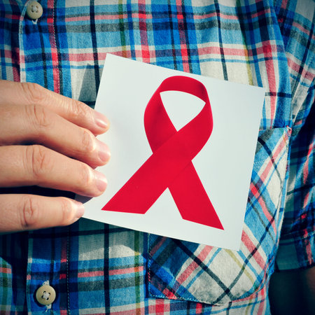 a young man holding a picture of a red ribbon, for the fight against AIDS, on his chest