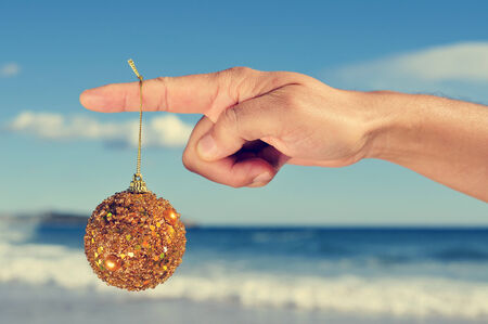 a golden christmas ball hanging in the forefinger young man on the beach, with a filter effectの写真素材