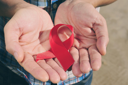 young man with a red awareness ribbon for the fight against AIDS in his hands, with a filter effectの写真素材