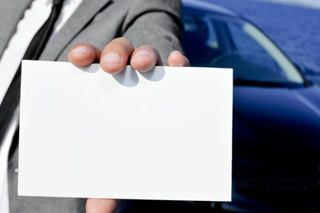 closeup of a man in suit holding a blank signboard with a car in the backgroundの写真素材