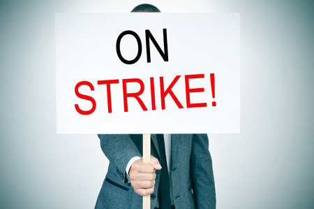a young man in suit with a protest signboard with the text on strike written in itの写真素材