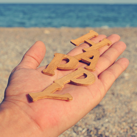 the hand of a young man showing wooden letters forming the word happy, on the beach, with a filter effectの写真素材
