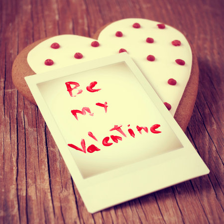 a heart-shaped biscuit and a instant photo with the text be my valentine on a wooden table, with a...
