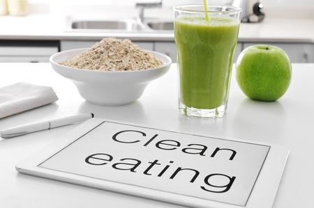 a tablet with the text clean eating written in it and a bowl with oatmeal cereal, a glass with a green smoothie and an apple on the kitchen table a tablet with the text clean eating written in it and a bowl with oatmeal cereal, a glass with a green smoothie and an apple on the kitchen table
