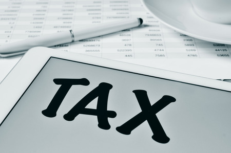 the word tax written in the screen of a tablet, on a table with a balance sheetの写真素材