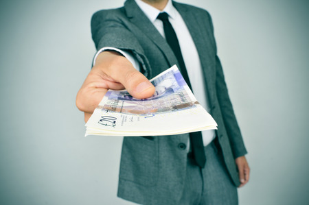 a young man in suit giving a wad of pound sterling bills to the observerの写真素材