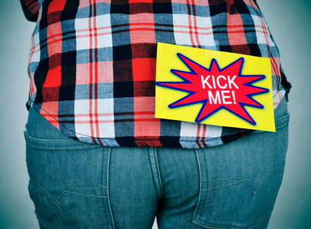 a young caucasian man wearing a plaid patterned shirt with a paper attached with tape to his back...