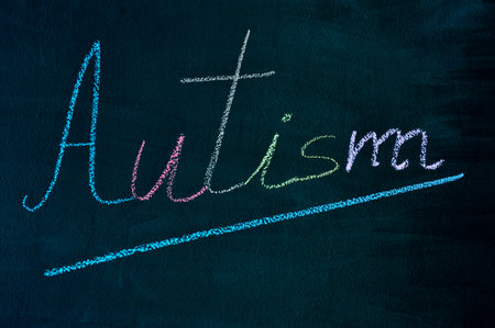 the word autism with its letters written with chalk of different colors on a green chalkboardの写真素材
