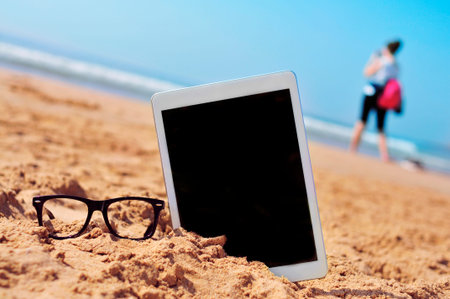 a pair of black plastic-rimmed eyeglasses and a tablet computer with a black blank space in the...